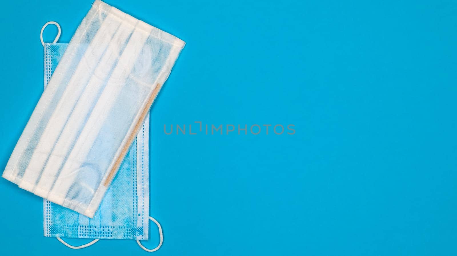 Two disposable surgical face masks with rubber pads to cover the mouth and nose on a blue background. The concept of protection from bacteria, healthcare and medicine. COVID-19. Copy space.