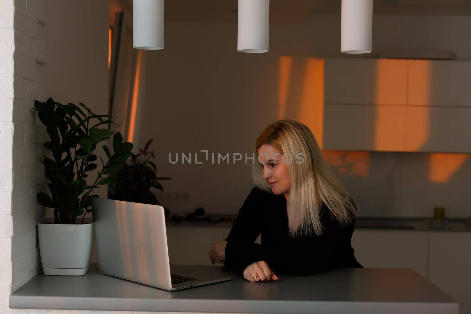 young pretty girl sitting near the window with a laptop, she uses the computer at home on the windowsill, a woman freelance, copy space for text