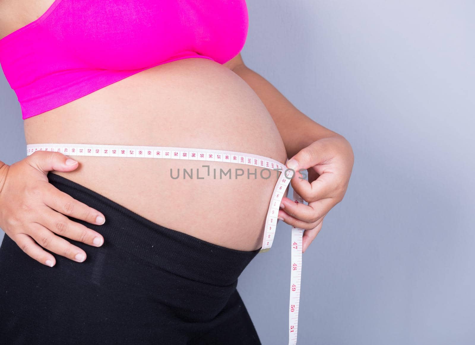 close-up belly of Pregnant woman with measuring tape on gray background by geargodz