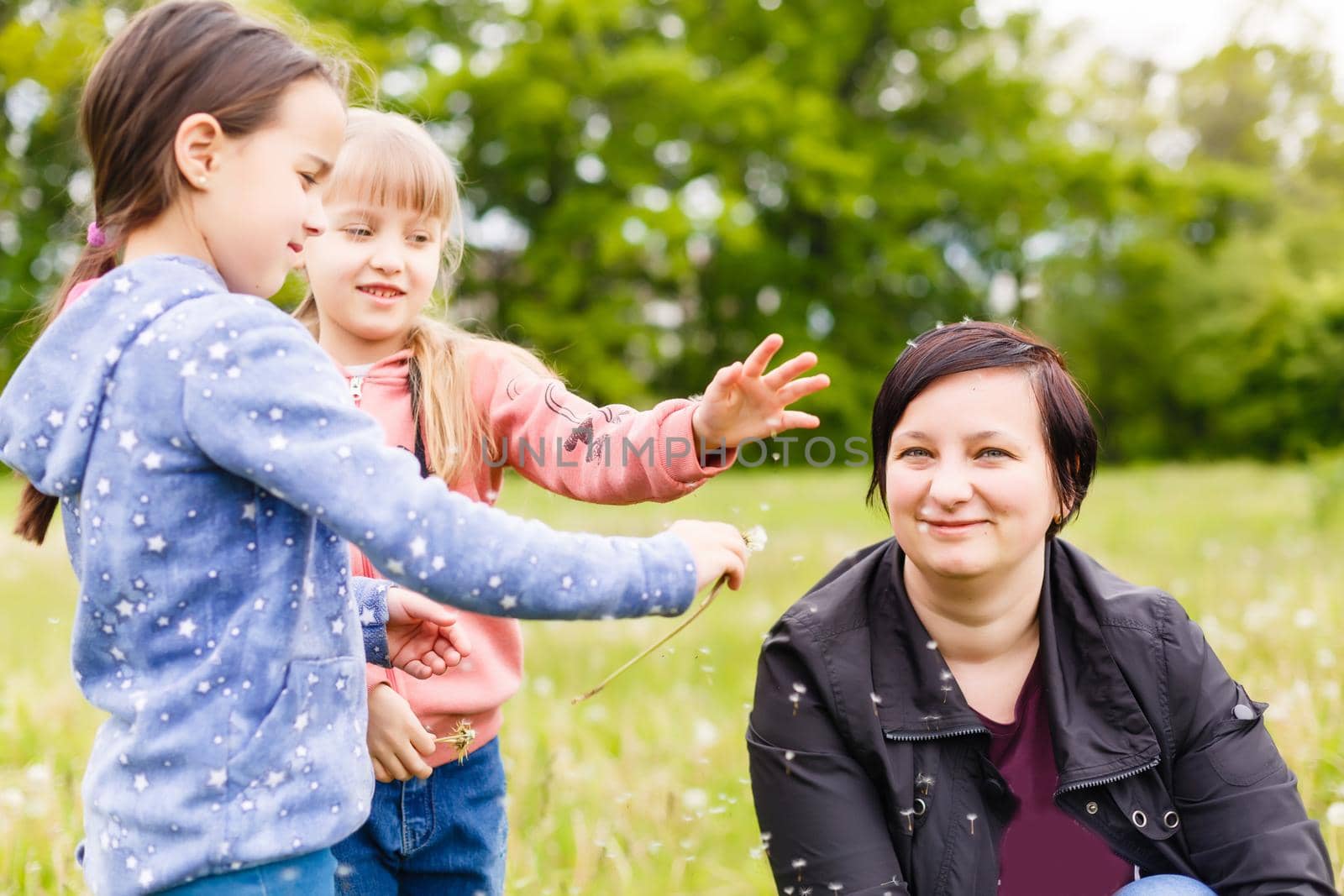 Mother with small daughter blowing to dandelion - lifestyle outdoors scene in park by Andelov13
