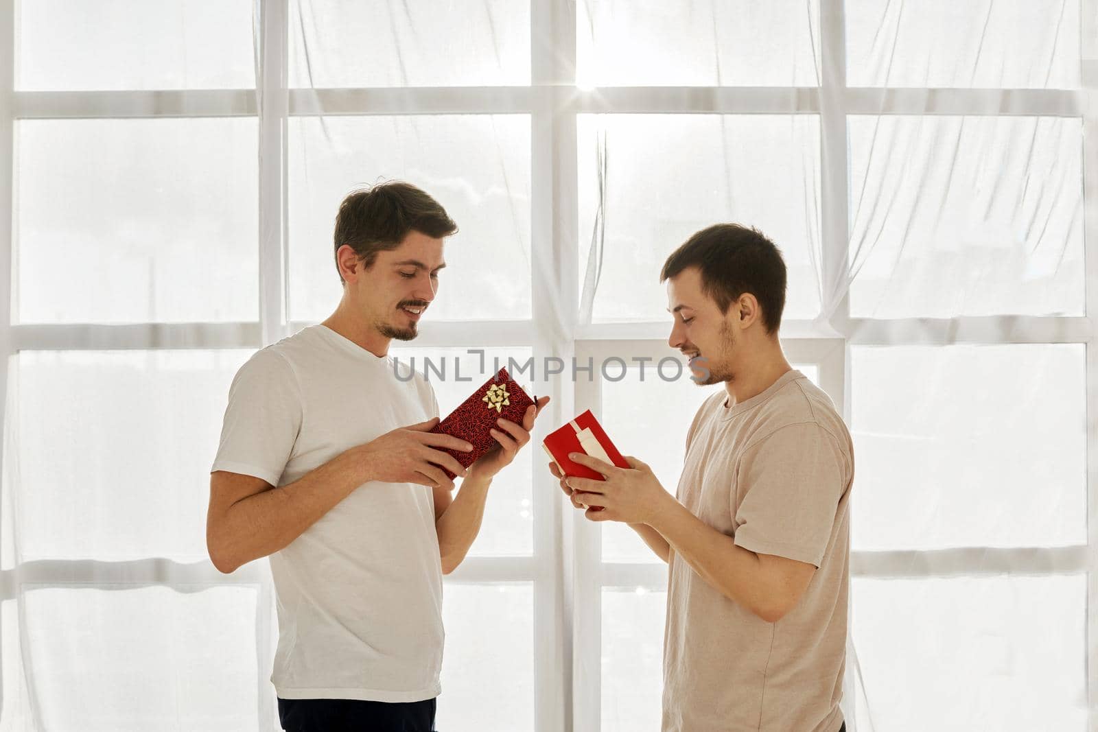 Gay couple of men exchanged gifts for a holiday at home against the background of a window. Two boyfriends in the morning