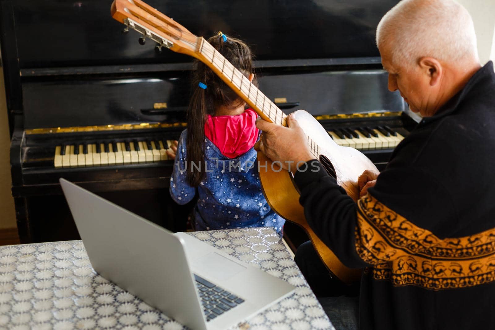 little girl plays piano together with grandfather, learning online on a laptop