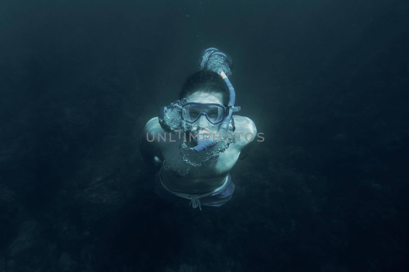 Young man in mask and snorkel swimming underwater in deep sea.