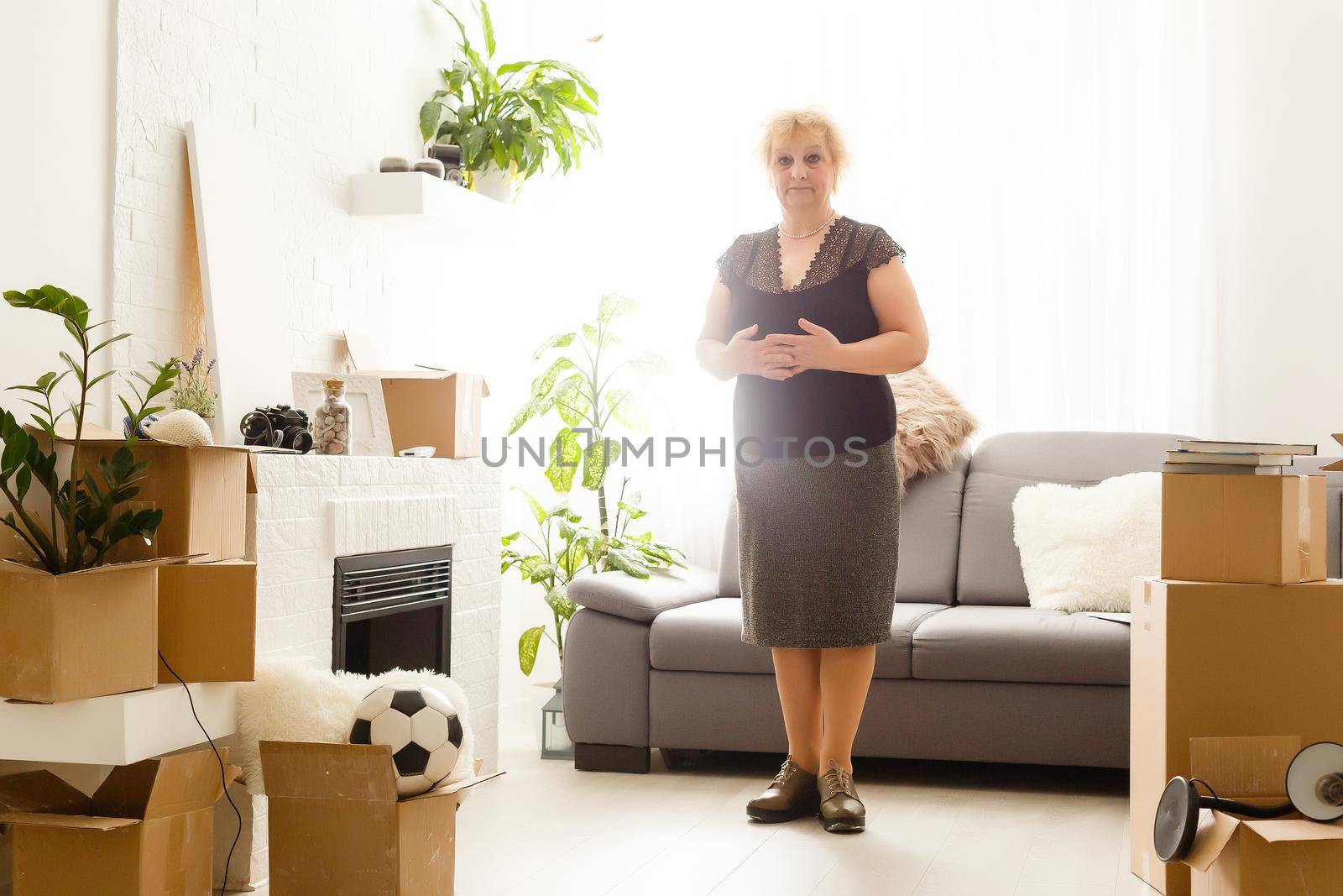 Happy excited mature retired middle aged woman standing in modern living room interior alone with arms outstretched enjoy freedom and wellbeing feel motivated at new furnished renovated home concept