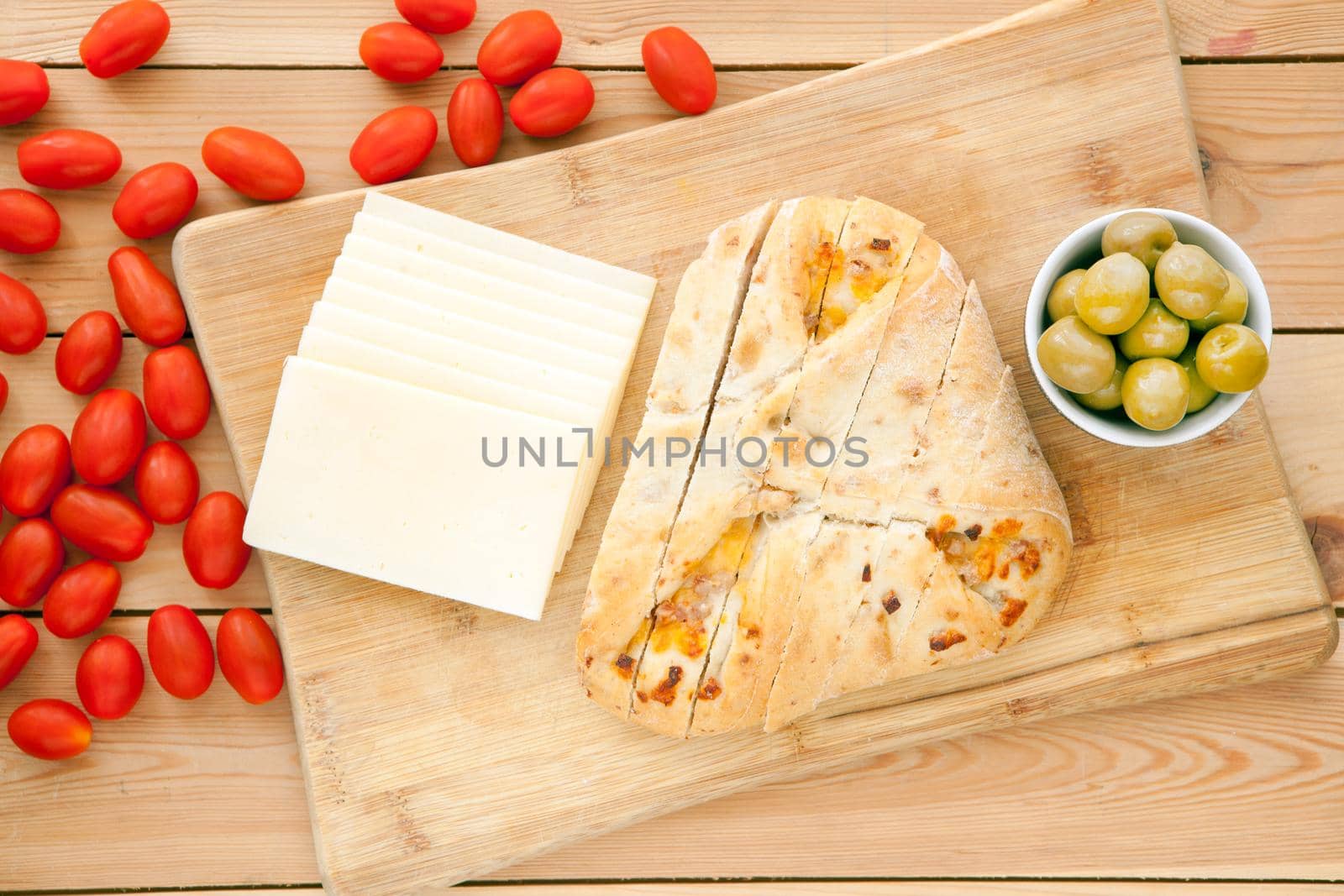 Fresh whole grain bread with cheese and green olives and tomatoes. Natural food concept. Loaf of organic bread on wooden background.