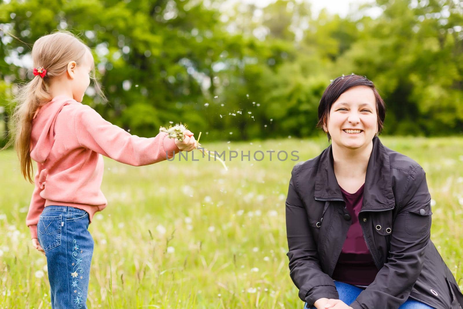 Mother with small daughter blowing to dandelion - lifestyle outdoors scene in park
