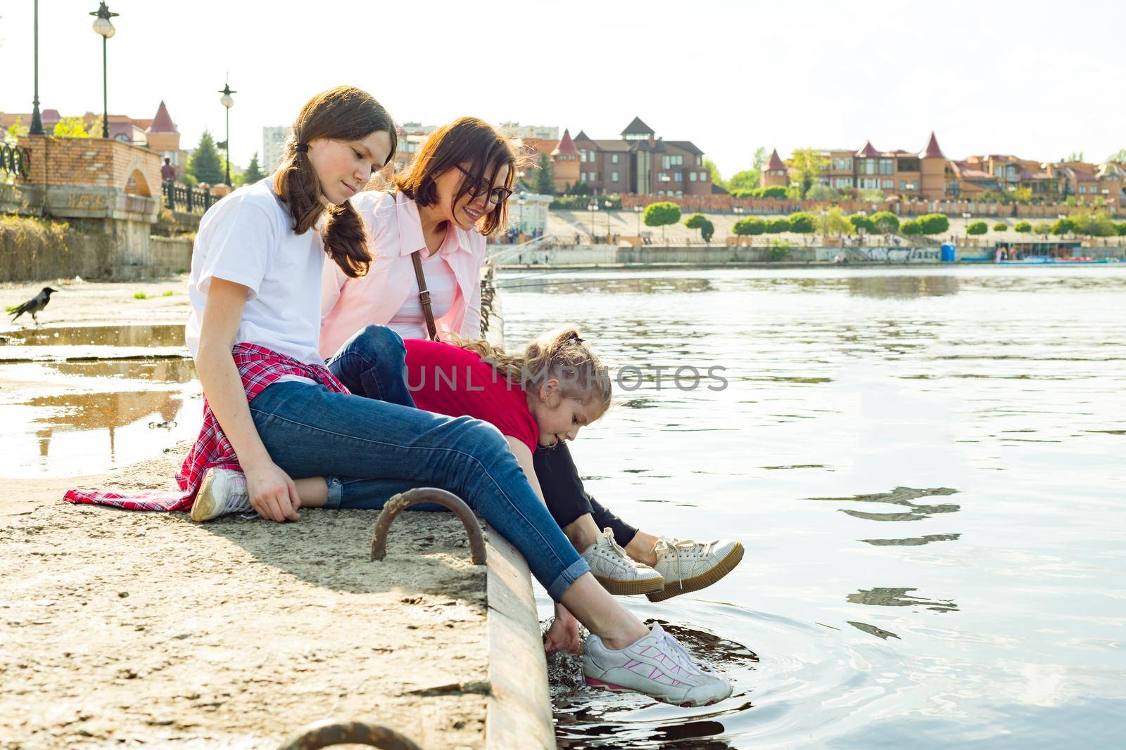 Outdoors portrait of mother and two daughters. Watching the water. Background nature, park, river.