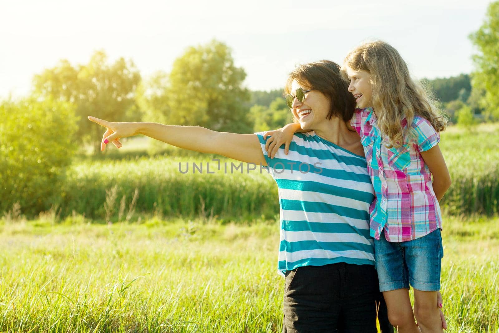 Beautiful mother outdoors with happy daughter child. A woman shows a little girl a finger in the distance. Loving family.