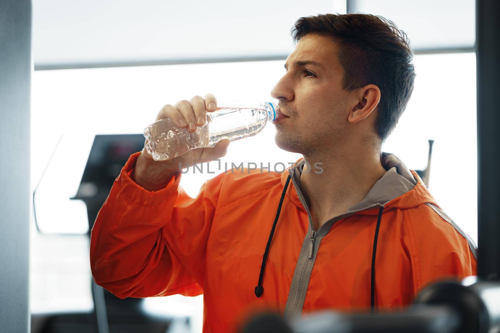 Portrait of young man drinking some water from a bottle in a gym by Fabrikasimf