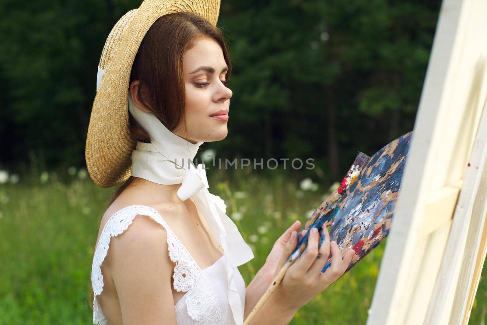 pretty woman in hat artist paints a picture on nature paint. High quality photo