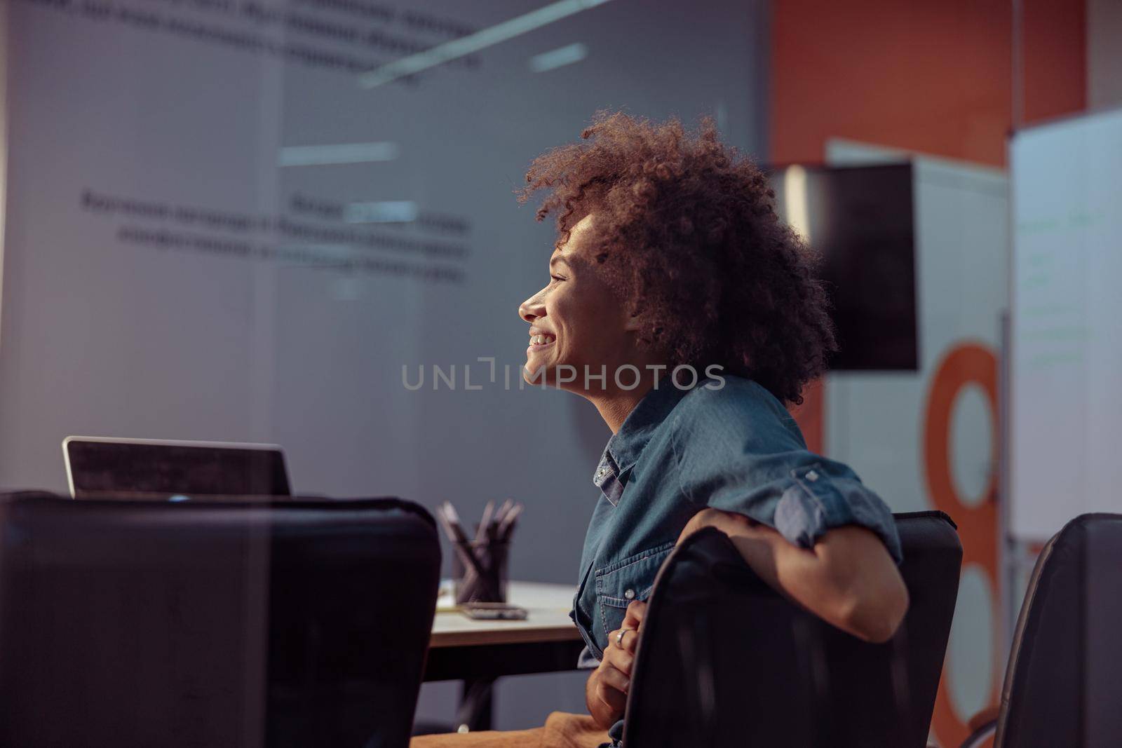 Smiling pretty multiethnic businesswoman sitting in the modern office by Yaroslav_astakhov