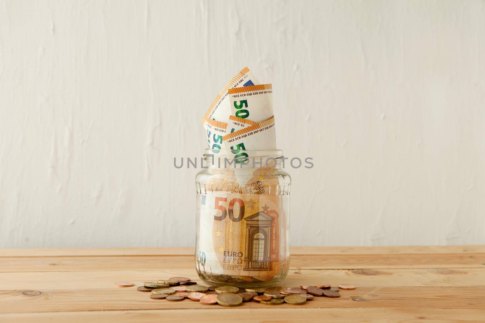 euro money banknotes in the glass jar at wooden table with euro coins or cents. Business concept. Money cash savings in glass pot at home.