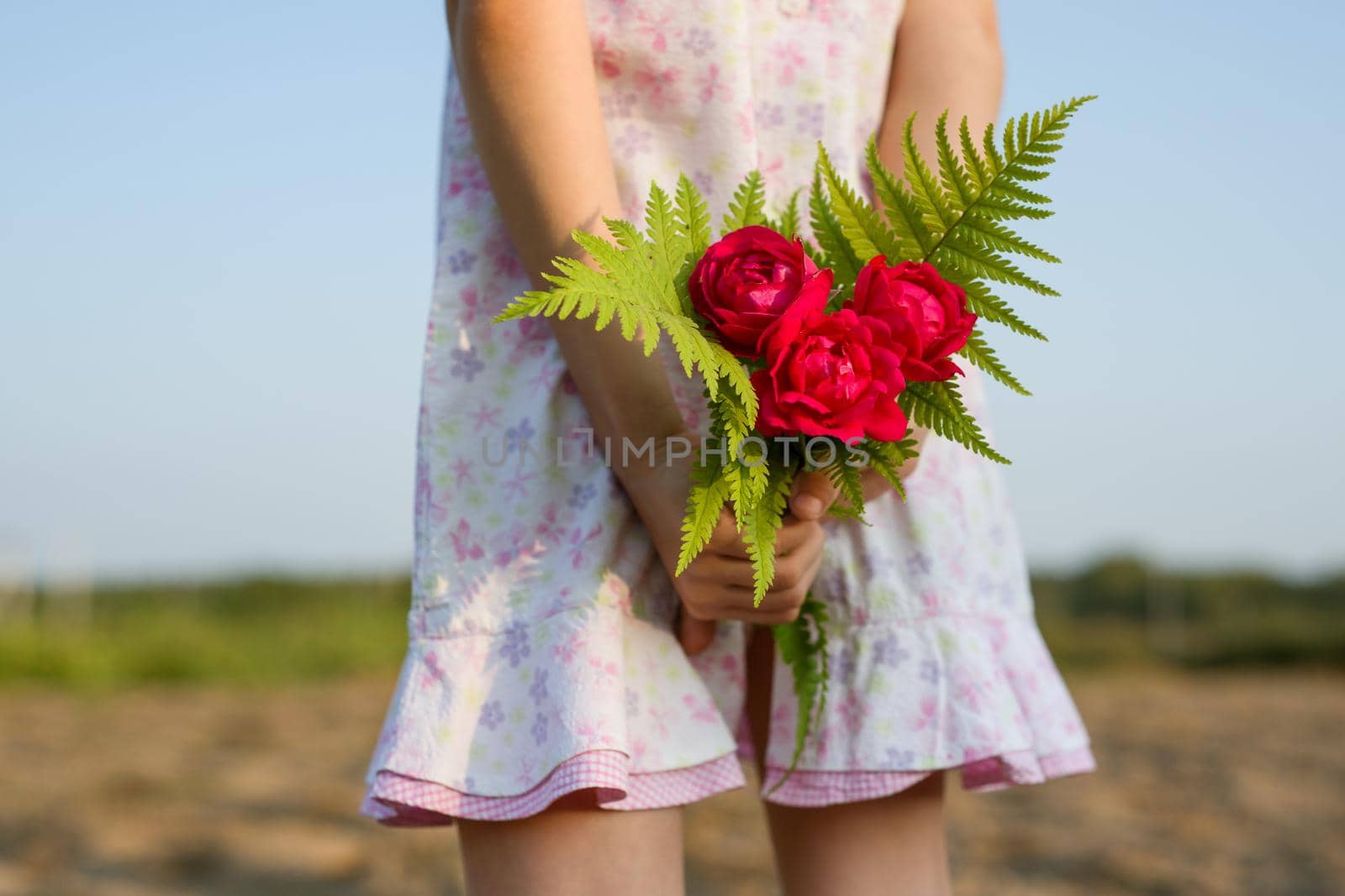 Little child girl holding bouquet of flowers. A bouquet behind your back.