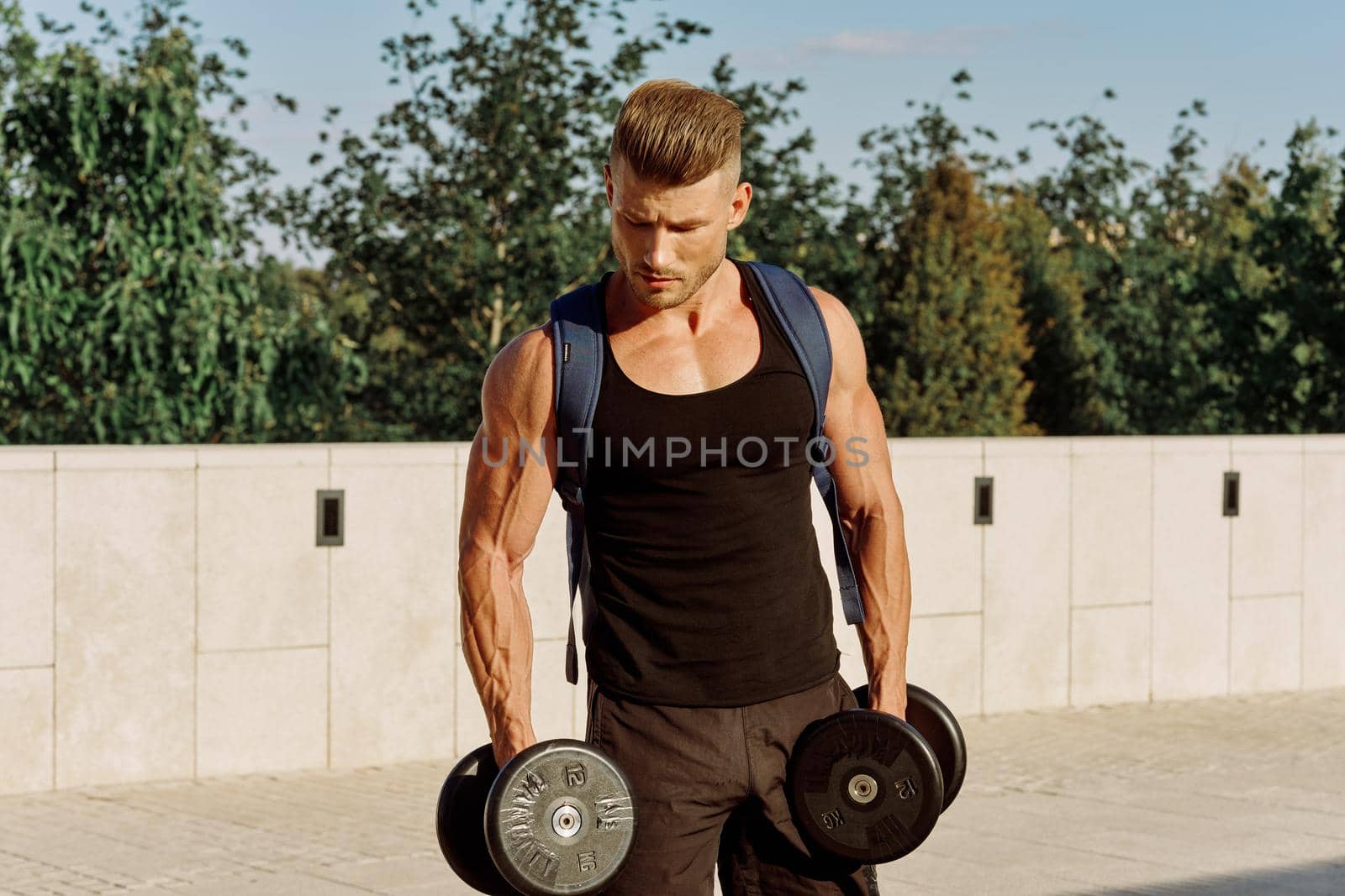 athletic man in black t-shirt with dumbbells in the park training by Vichizh