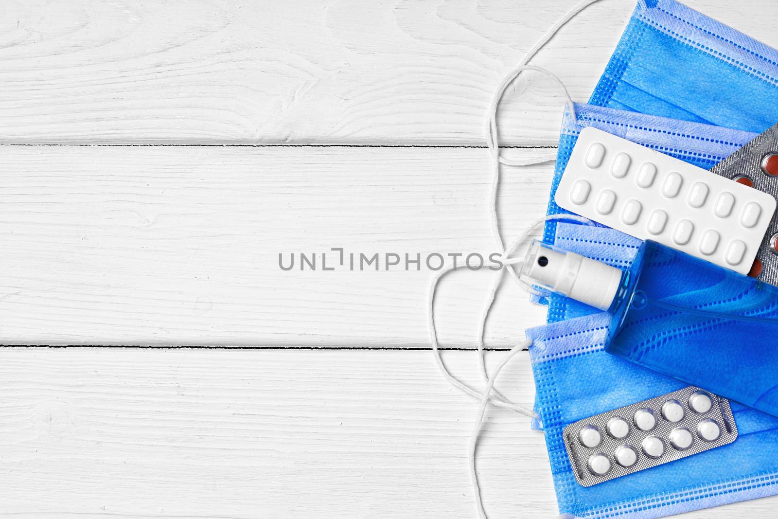 Blue face mask, pills and sanitizing gel on wooden background, copy space