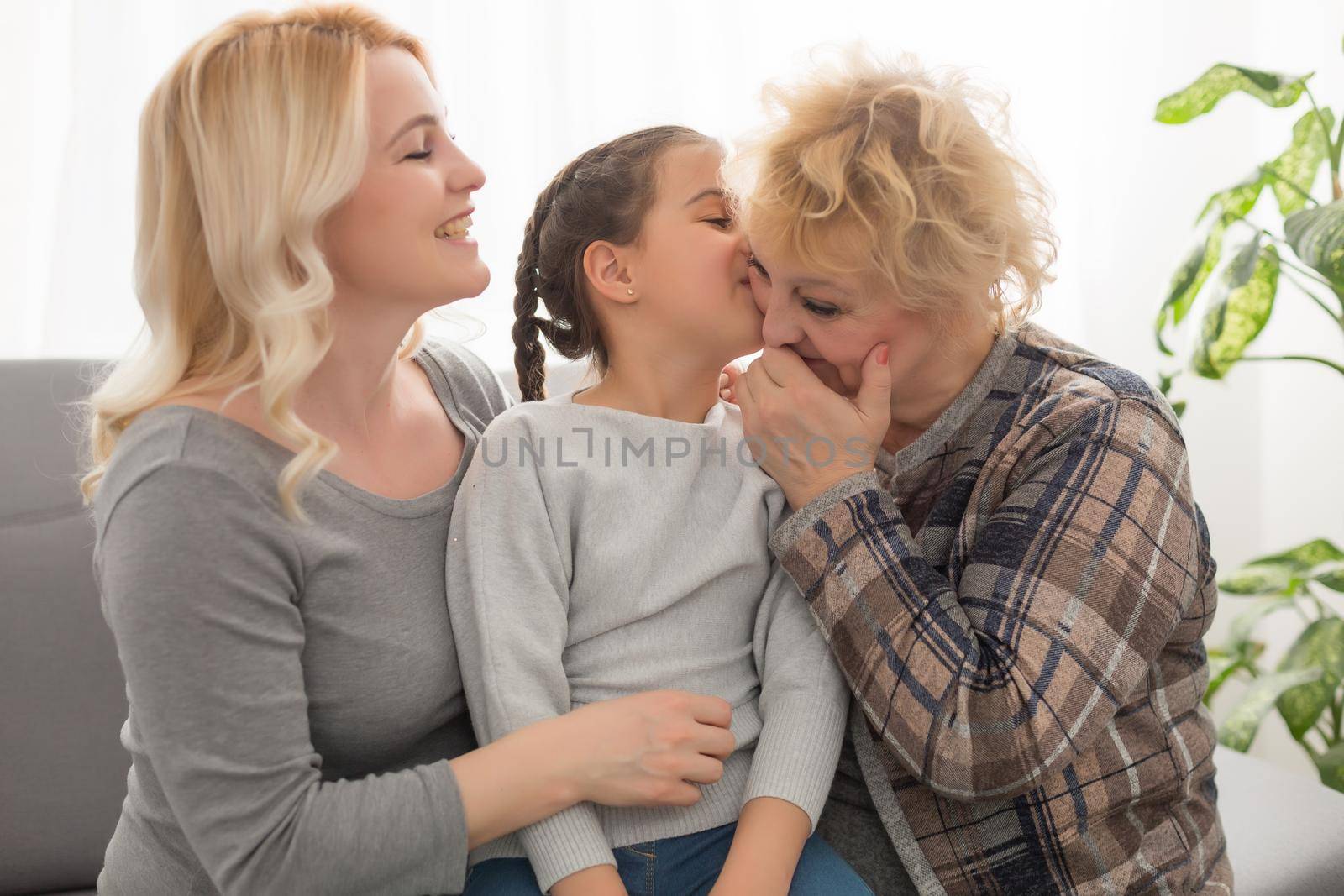 Three generations of women. Beautiful woman and teenage girl are kissing their granny while sitting on couch at home