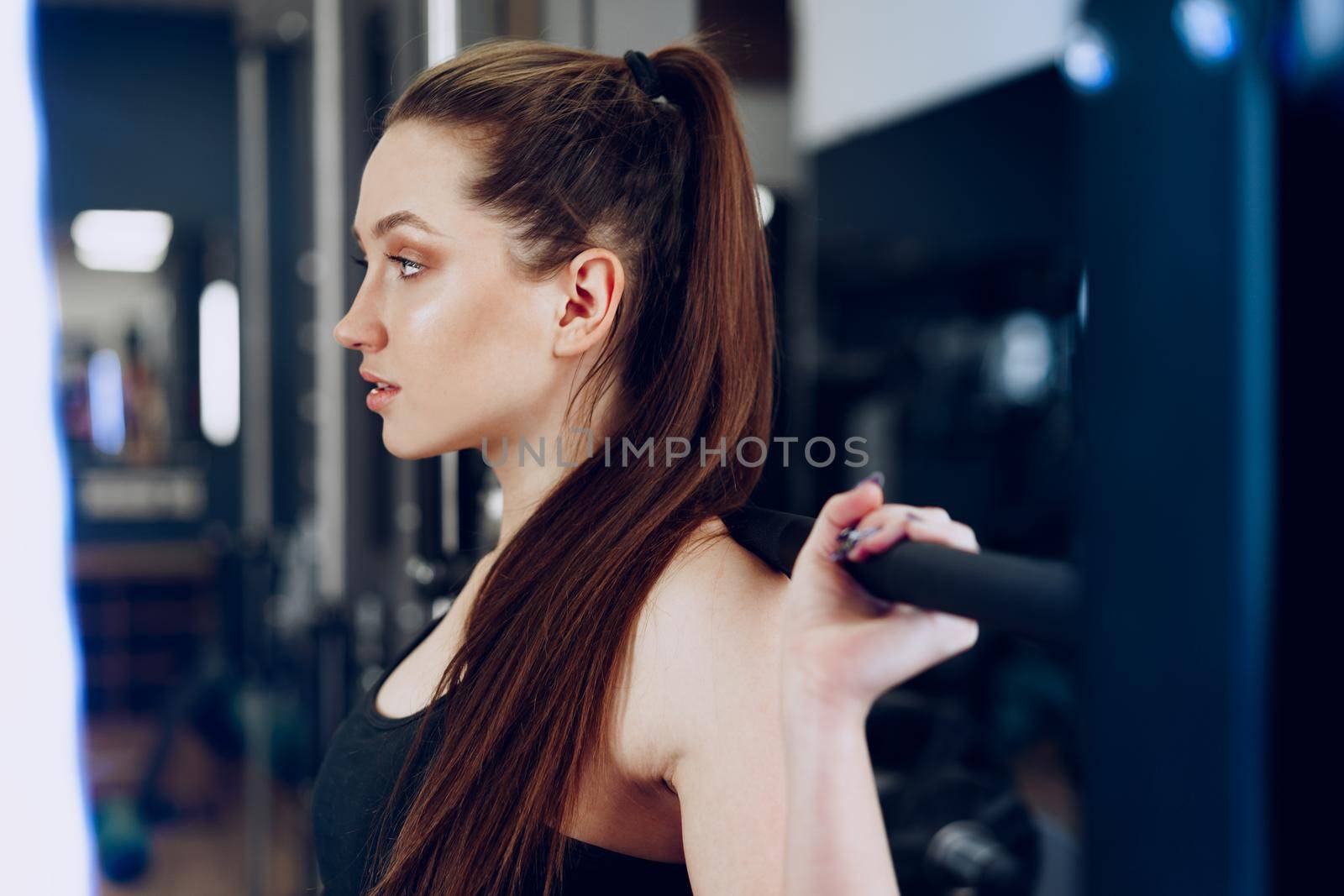 Young woman doing squats with barbell in a gym apparatus close up