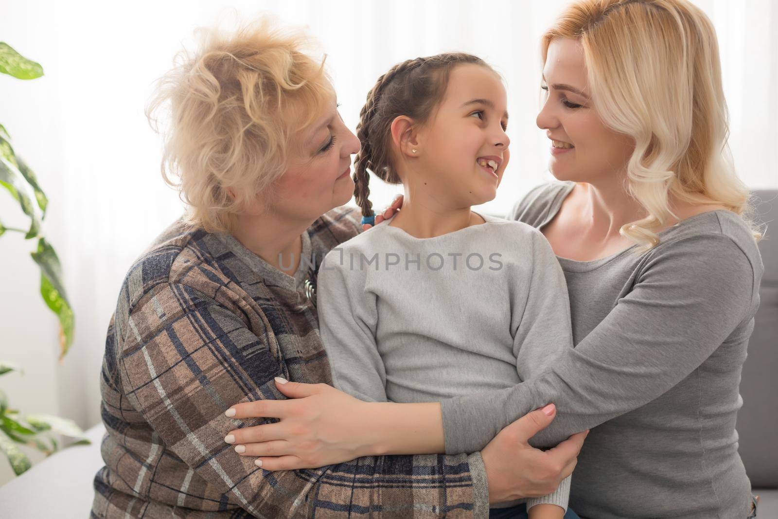 Portrait of three generations of women look at camera posing for family picture, cute little girl hug mom and granny enjoy time at home, smiling mother, daughter and grandmother spend weekend together