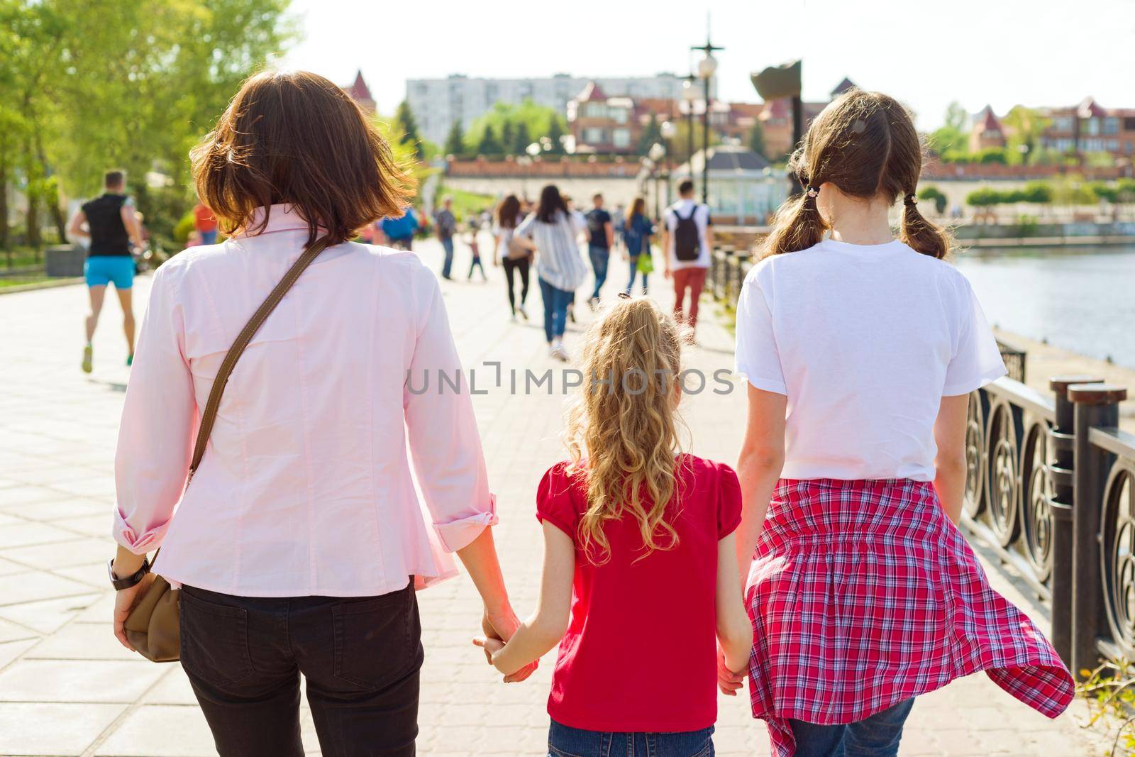 Outdoors portrait of mother and two daughters. Holding hands walking down the street, back view.