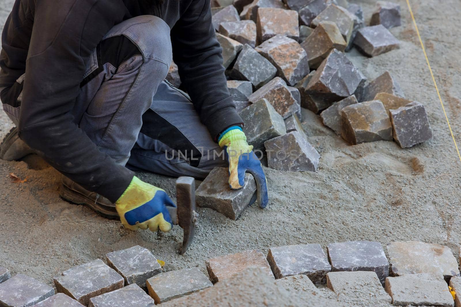 Road master in gloves lays paving stones in layers stone road by professional worker using stones and hammer by ungvar