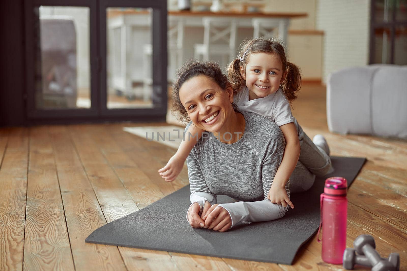 Waist up portrait of smiling woman and girl lying on mat at home while doing training