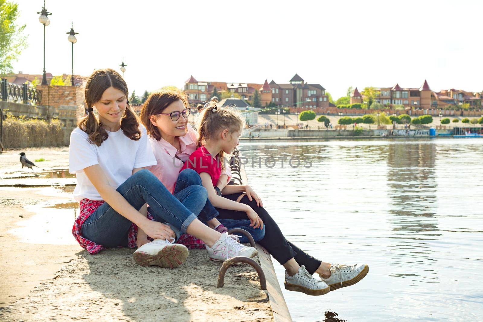 Outdoors portrait of mother and two daughters. Watching the water. Background nature, park, river.