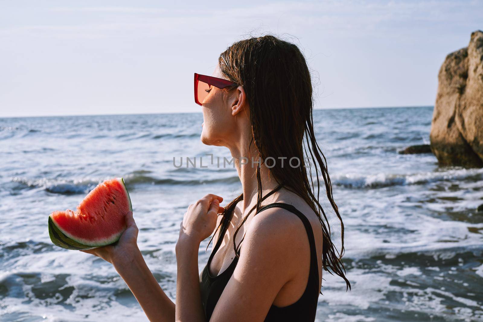 cheerful woman in black swimsuit eating watermelon on the beach. High quality photo