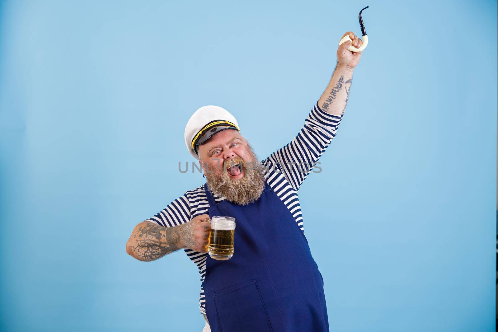 Excited obese man sailor holds beer and raises up pipe on light blue background by Yaroslav_astakhov