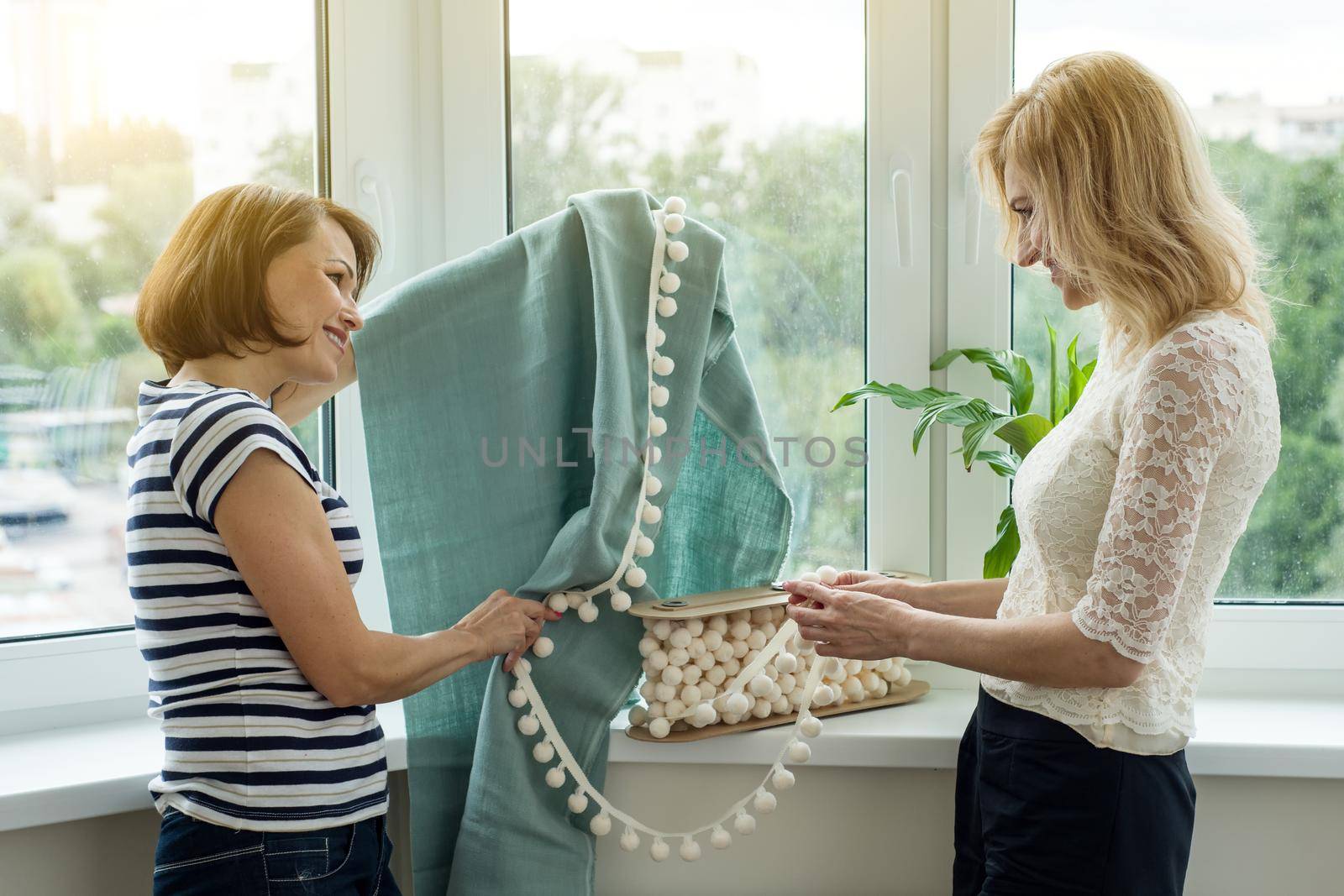 Interior designer shows samples of fabrics and accessories for curtains in the new house. Picture in the window background.