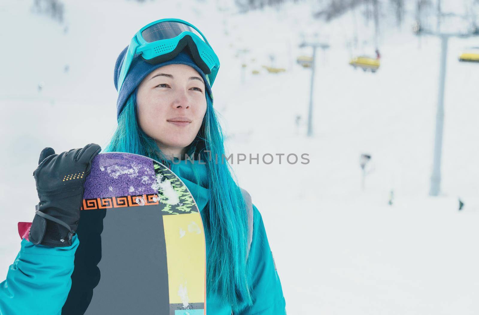 Young woman with blue hair standing with snowboard on ski resort
