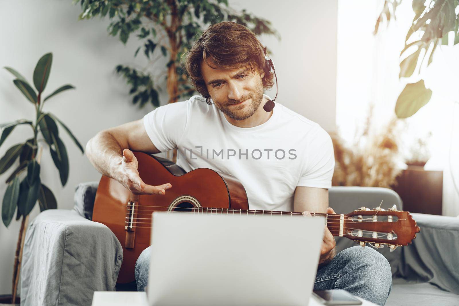 Young man watching guitar tutorial on his laptop at home