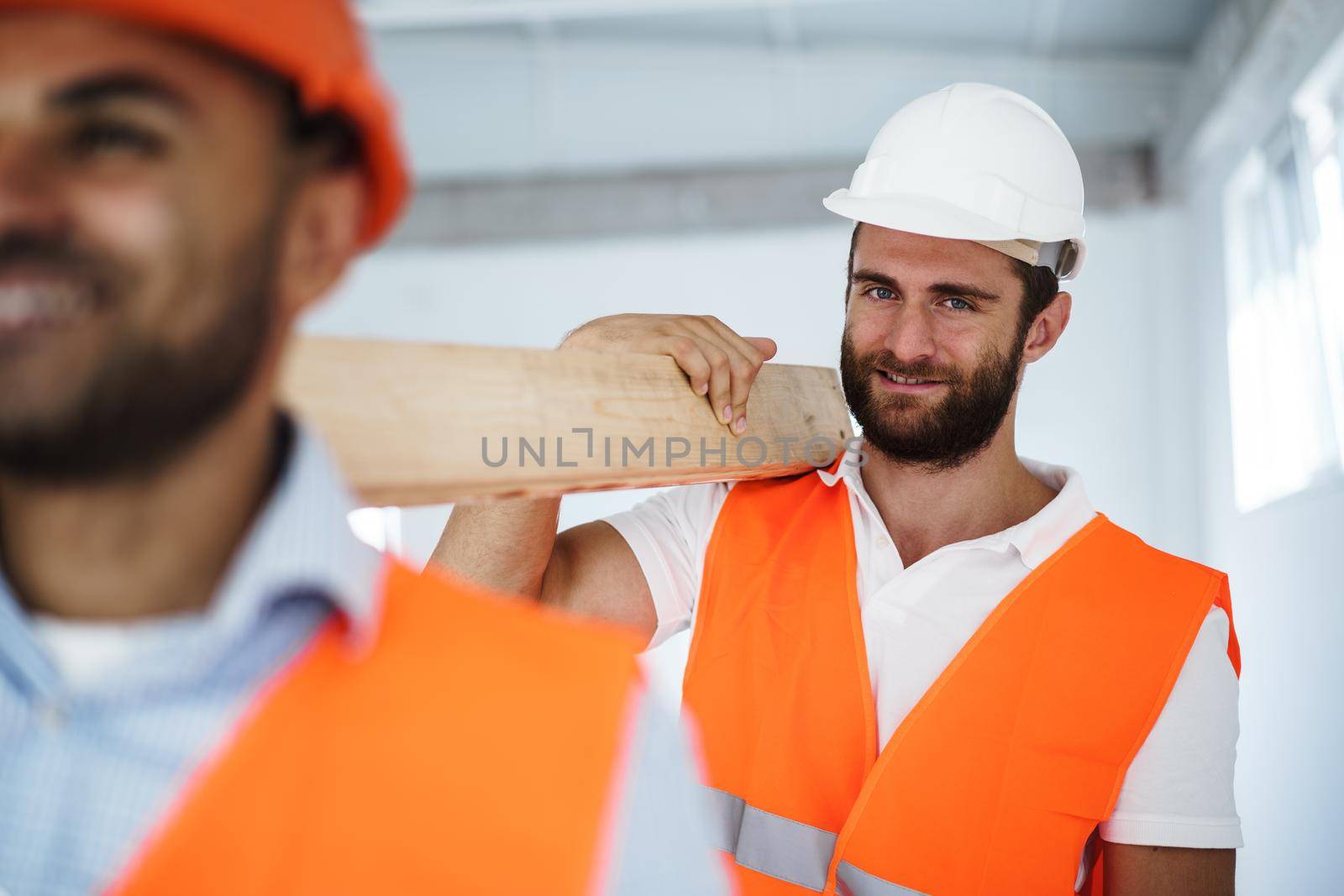 Two young men builders carrying wood planks on construction site, close up photo