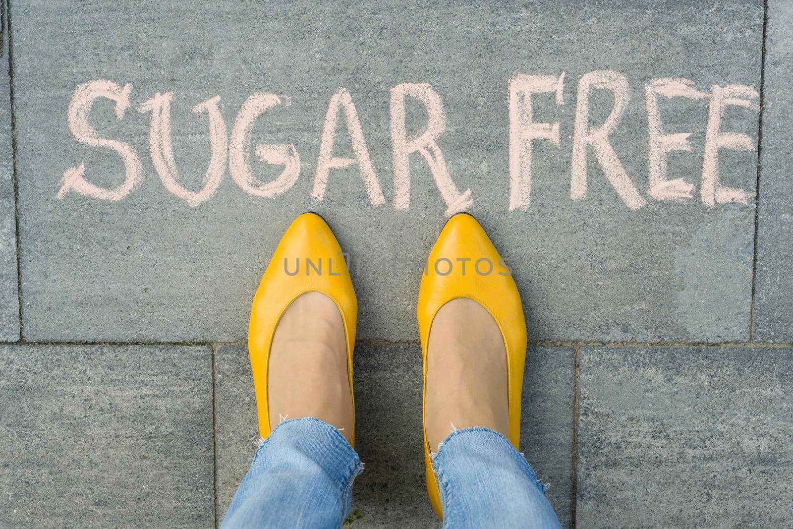 Female feet with text sugar free written on grey sidewalk.