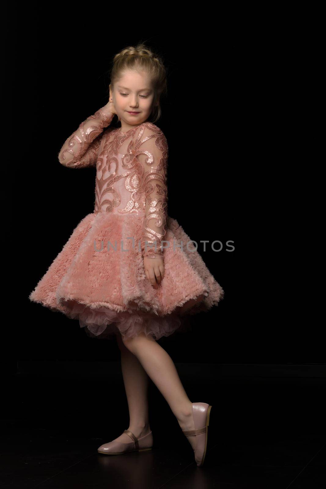A beautiful little girl straightens her hair on her head. The concept of beauty and fashion, photo on the cover of the magazine.Studio portrait on black background.