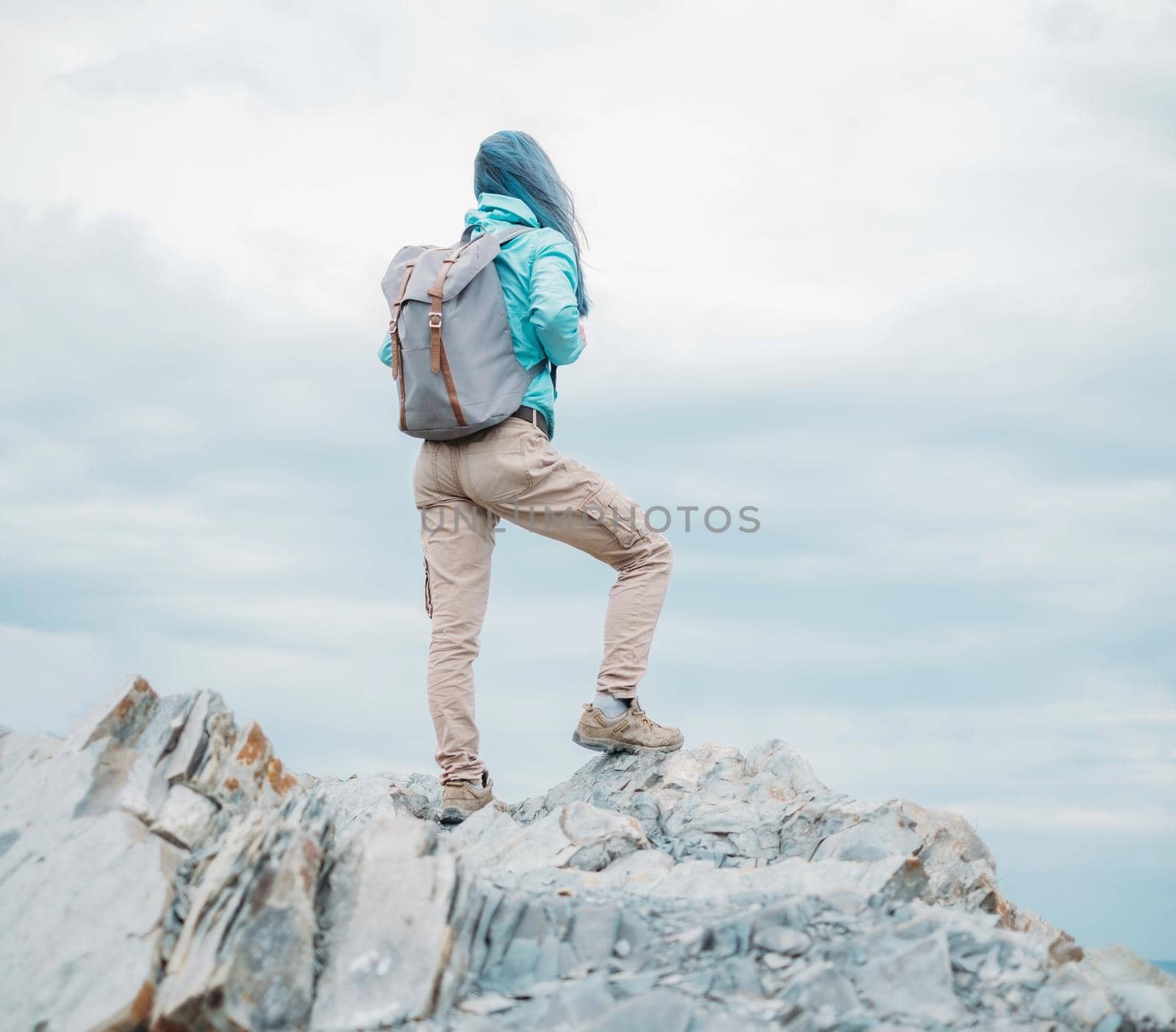 Unrecognizable explorer young woman with backpack standing on peak of cliff and looking into the distance