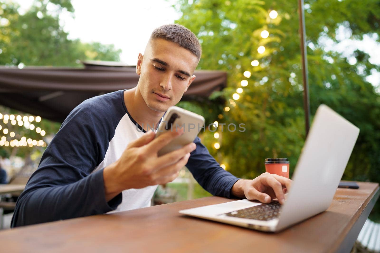 Young man using smartphone while sitting at outdoor cafe, close up