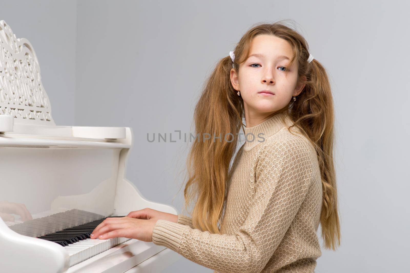 Beautiful teenage girl playing grand piano. Pretty girl in stylish clothes learning to play music instrument. Teenage child looking at camera