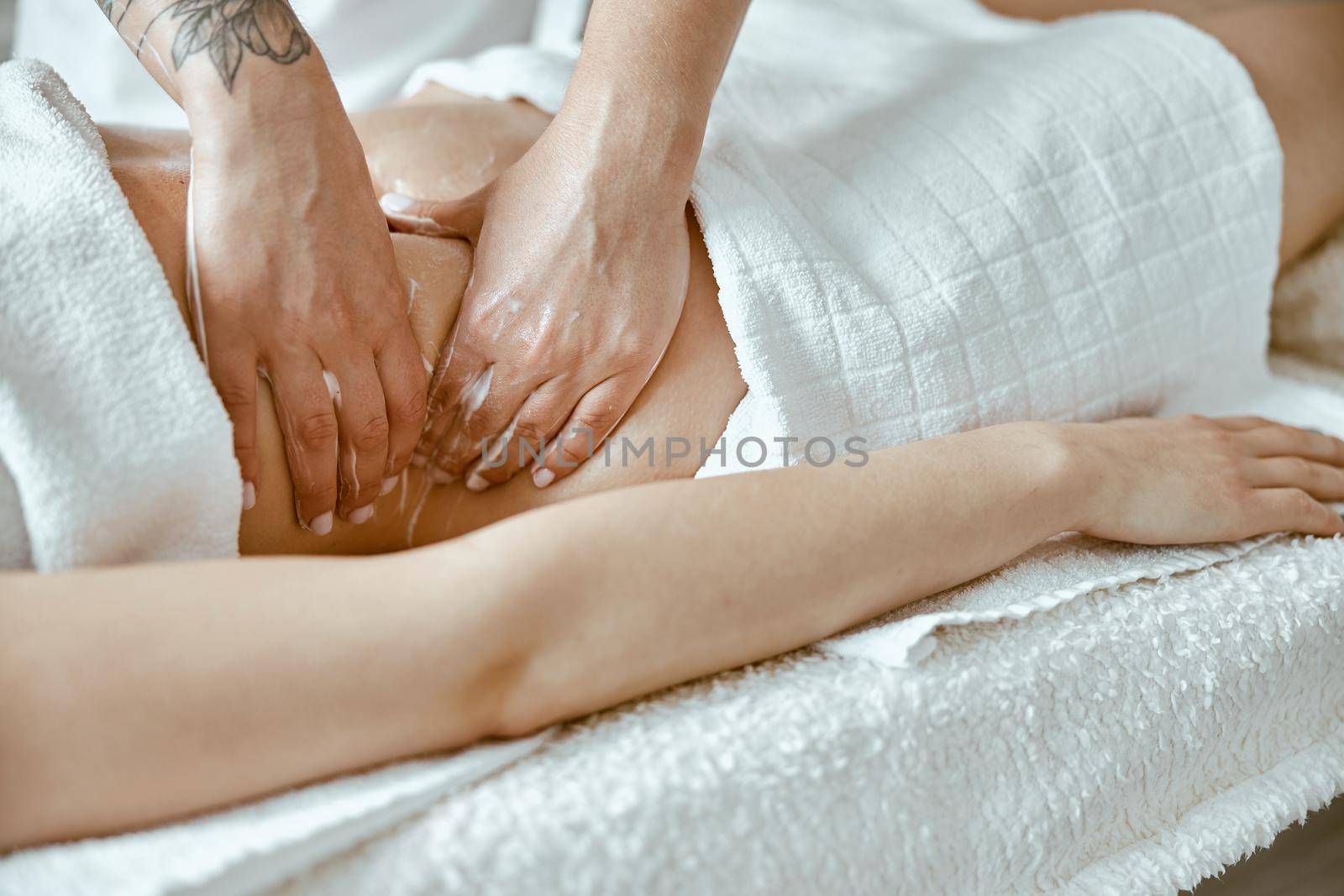 Professional massagist is doing stomach massage to young female client in modern wellness salon
