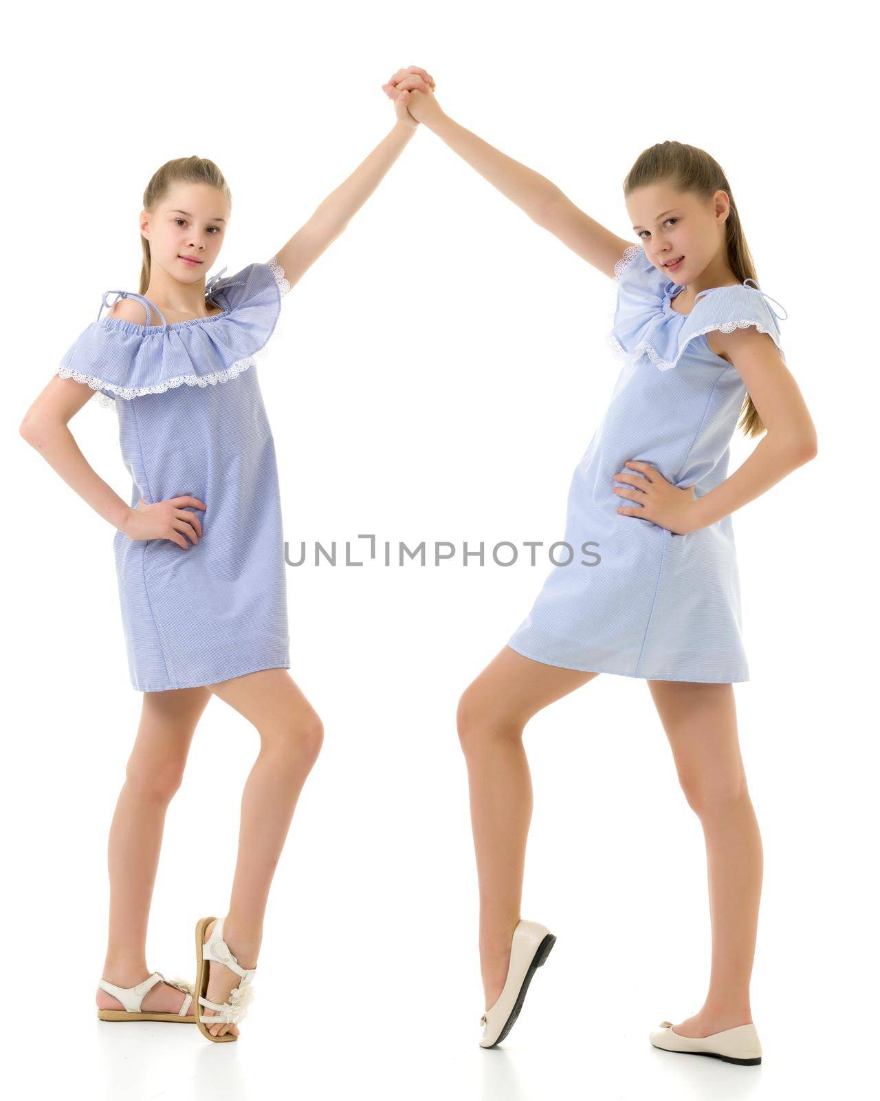 Two Pretty Twin Sisters in Identical Light Blue Dresses Holding Each Other Hand and Raising it over their Head, Beautiful Girls in Fashionable Clothes Posing in Studio Against White Background