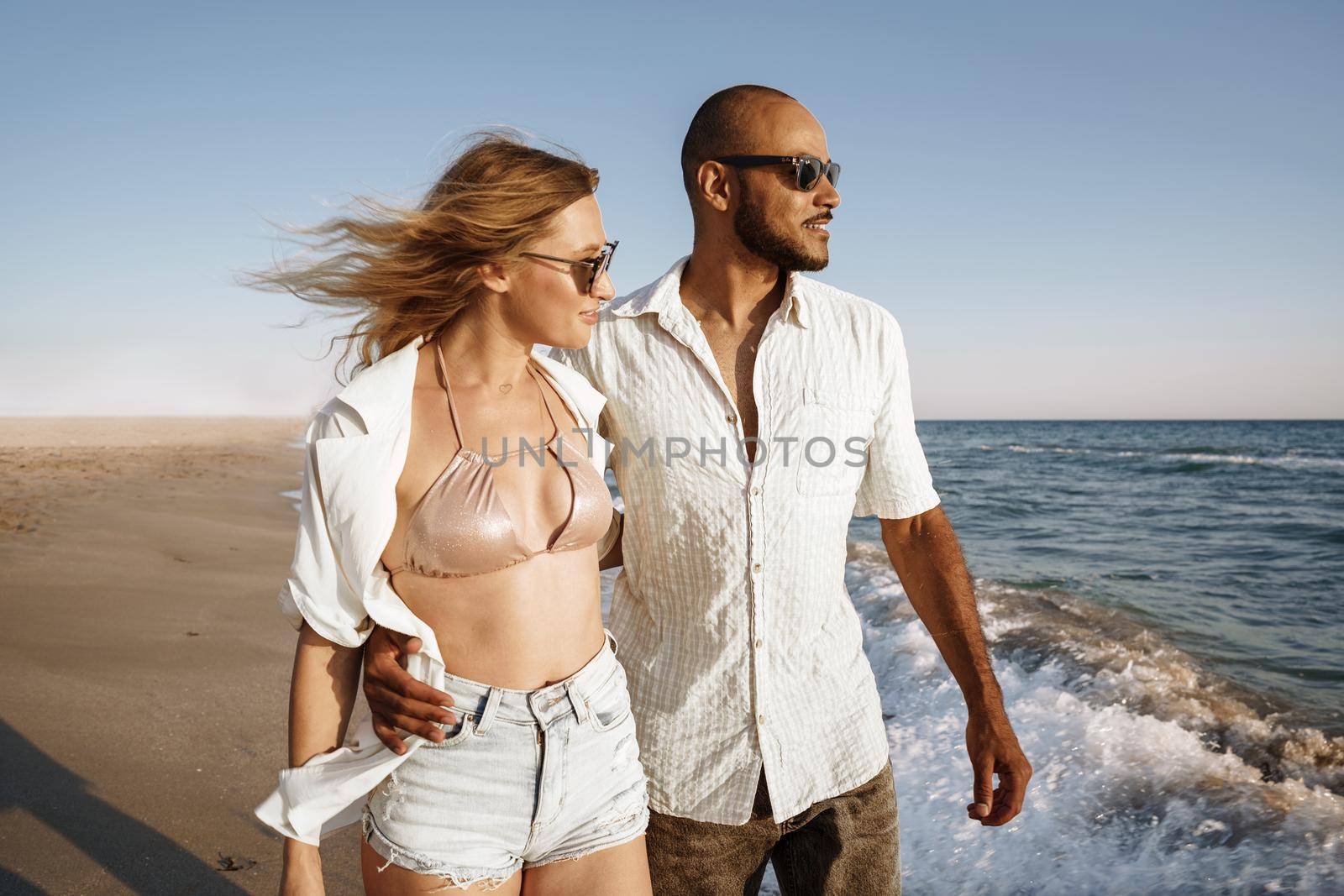 Young beautiful couple walking on beach near sea at sunset