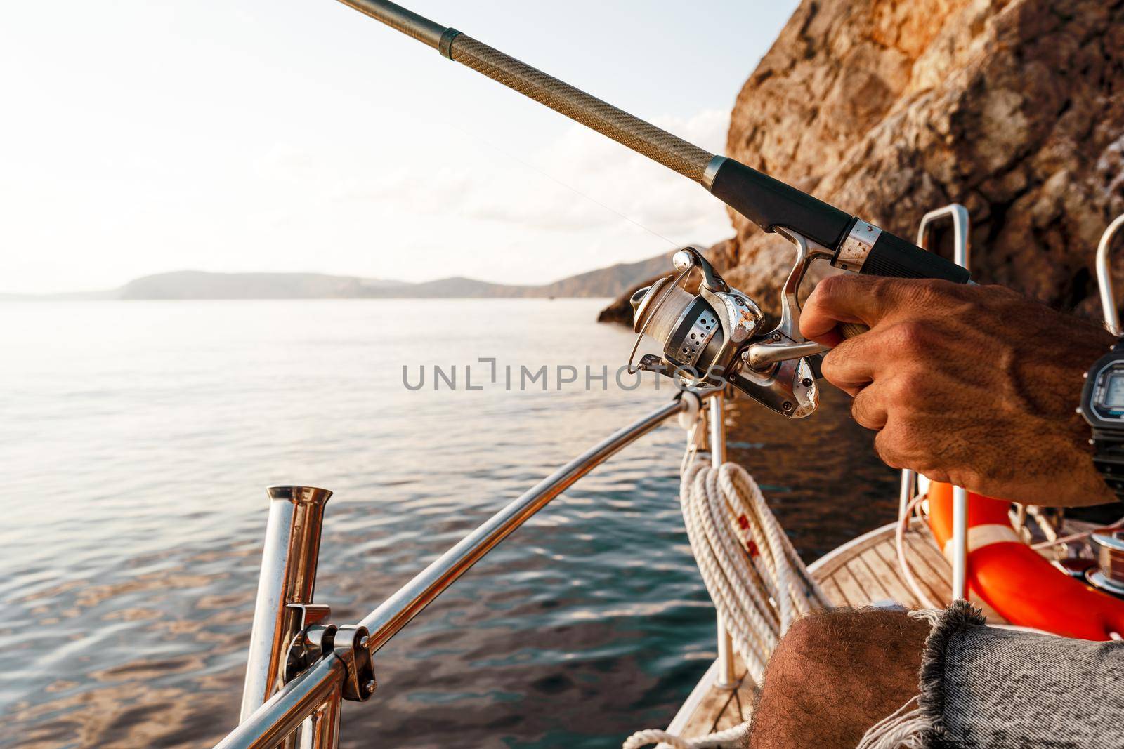 Close up photo of male hands holding fishing rod while fishing on sailboat in open sea