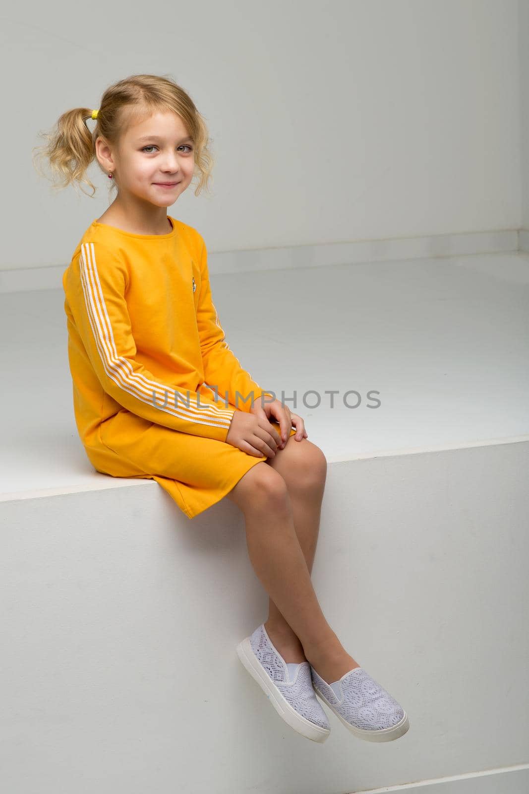 Beautiful little girl sits in a studio on a white podium. Style and fashion concept.