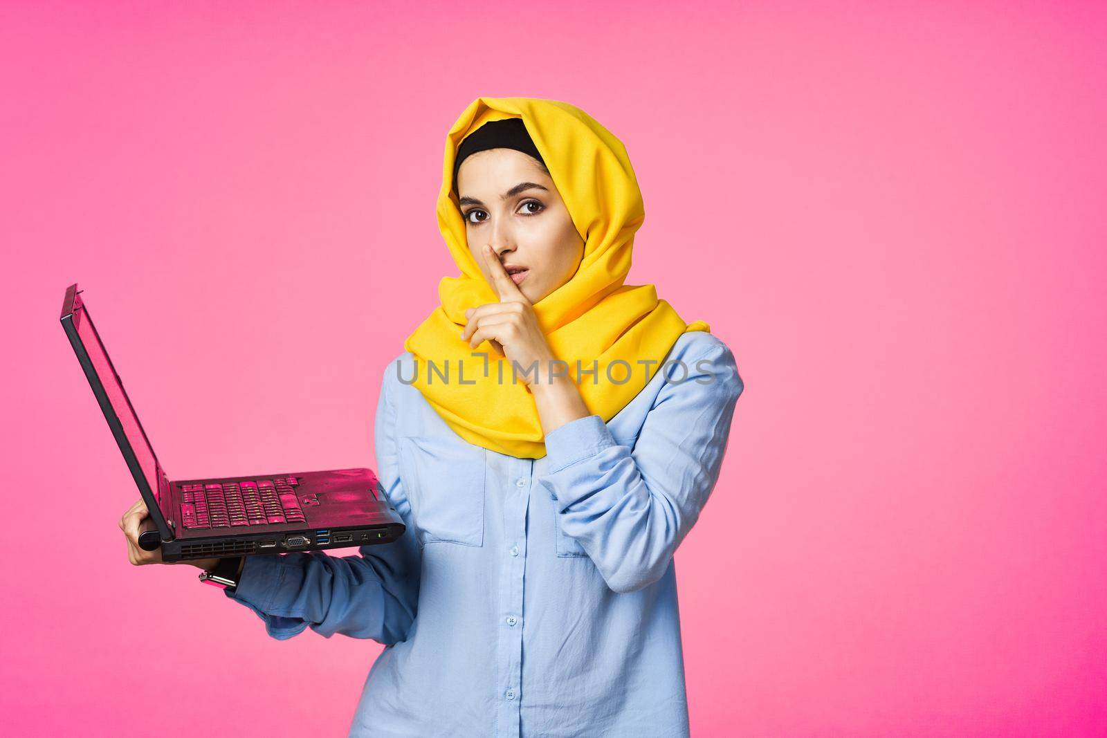 muslim woman in yellow hijab with laptop technology student pink background. High quality photo