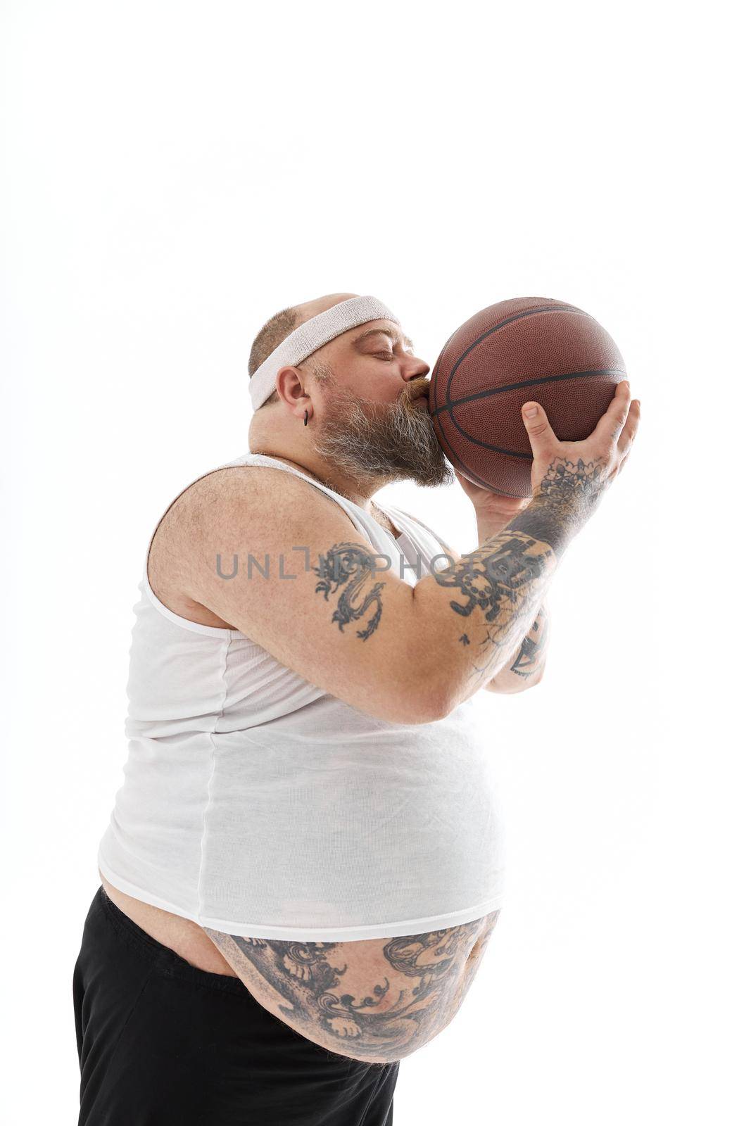 bearded fat caucasian tattoed man with basketball ball in white background. He is funny and happy by Yaroslav_astakhov