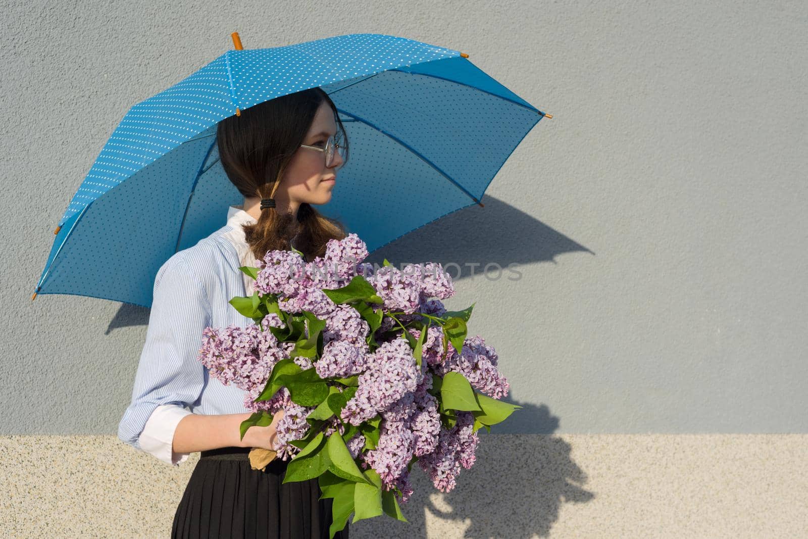 Profile portrait romantic teenage girl with bouquet of lilacs, with an umbrella on gray wall background. Outdoor, copy space
