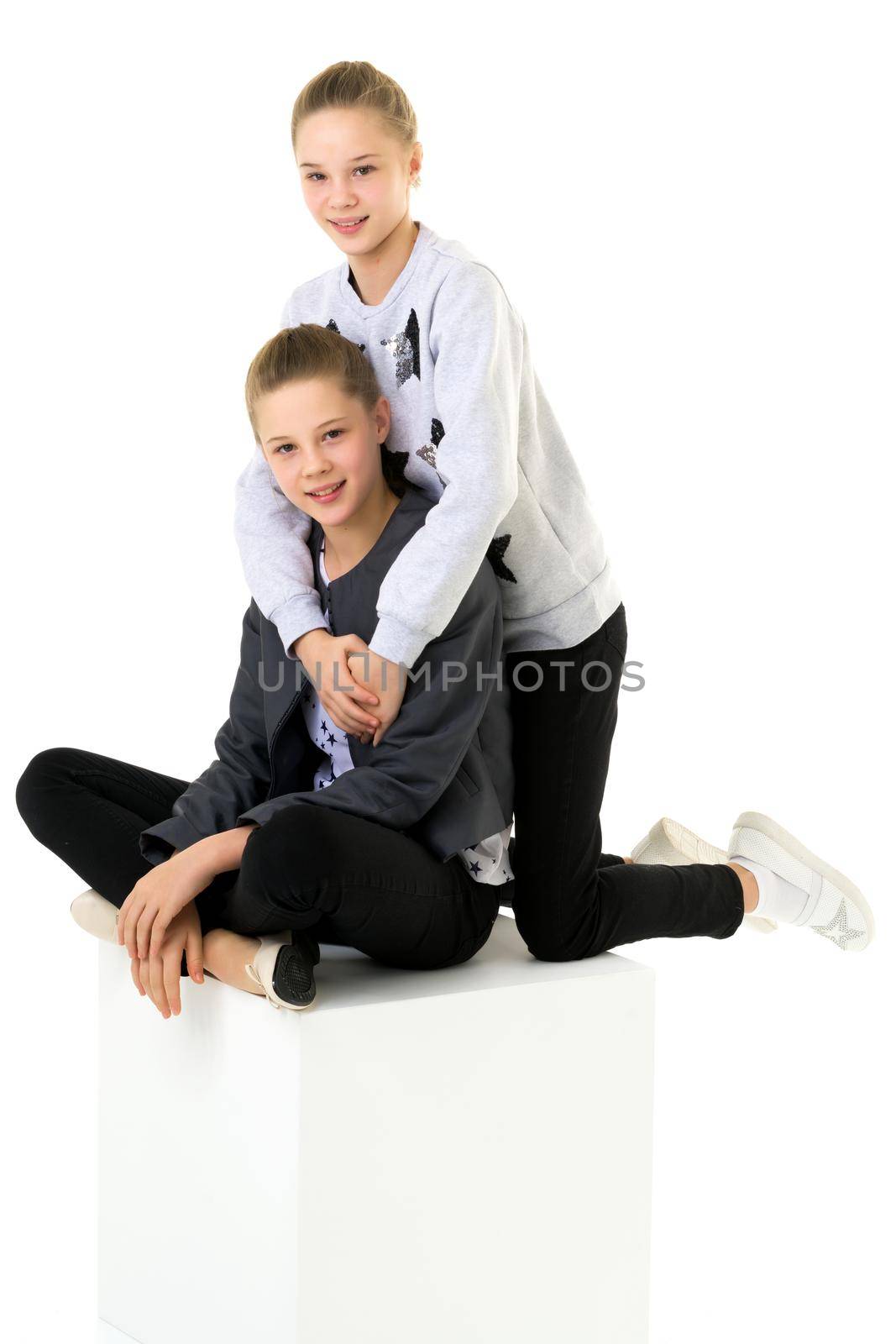 Smiling teenage girls in trendy stylish outfit posing together on a white background in the studio, portrait of cute twin sisters.
