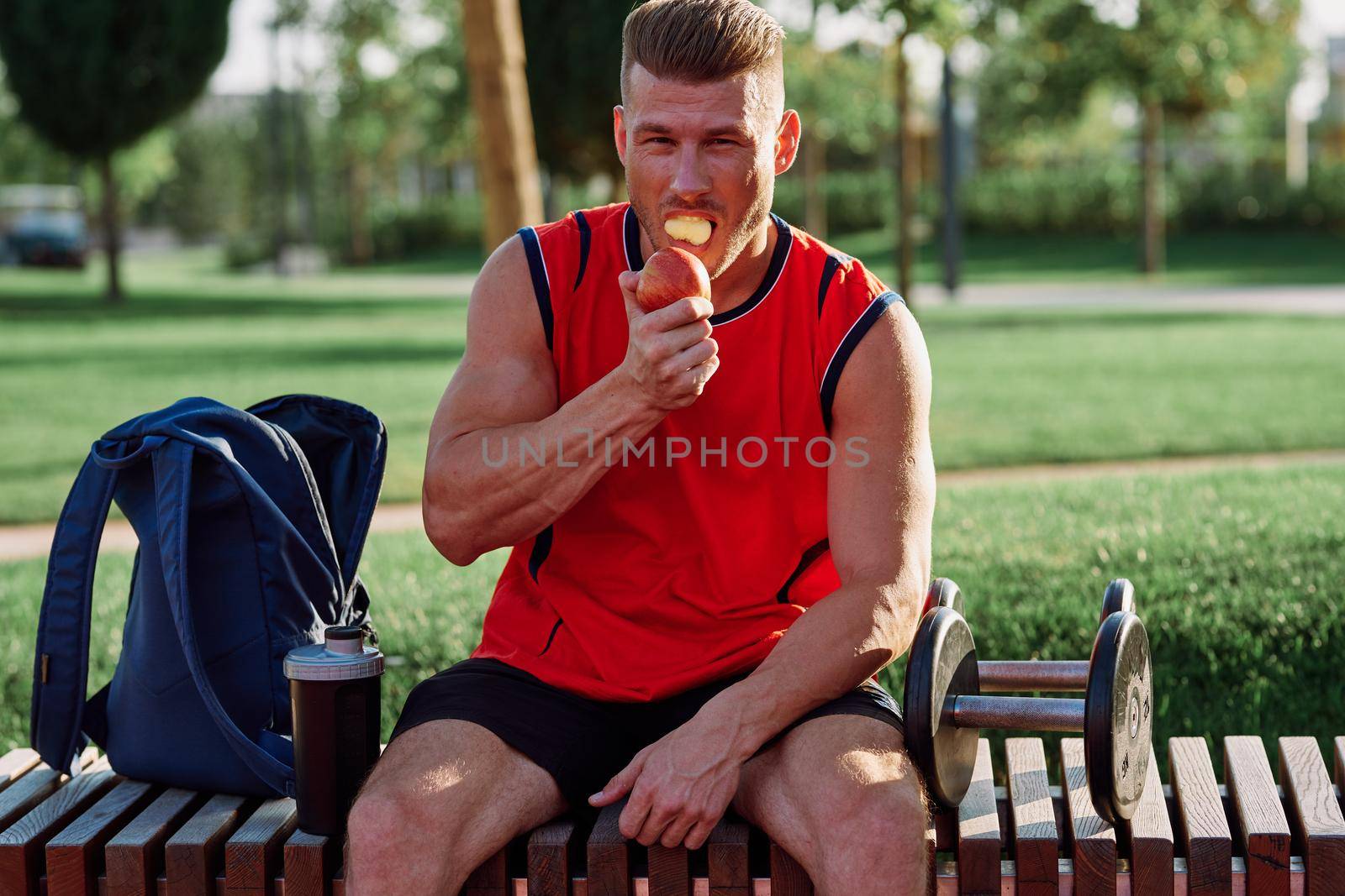 man in the park sits on a bench and eats an apple summer by Vichizh
