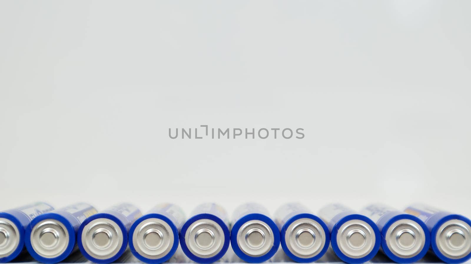 Lots of AA alkaline batteries on a white glossy background with reflection with copy space lined up in one line. Ukraine, Kiev - January 7, 2021