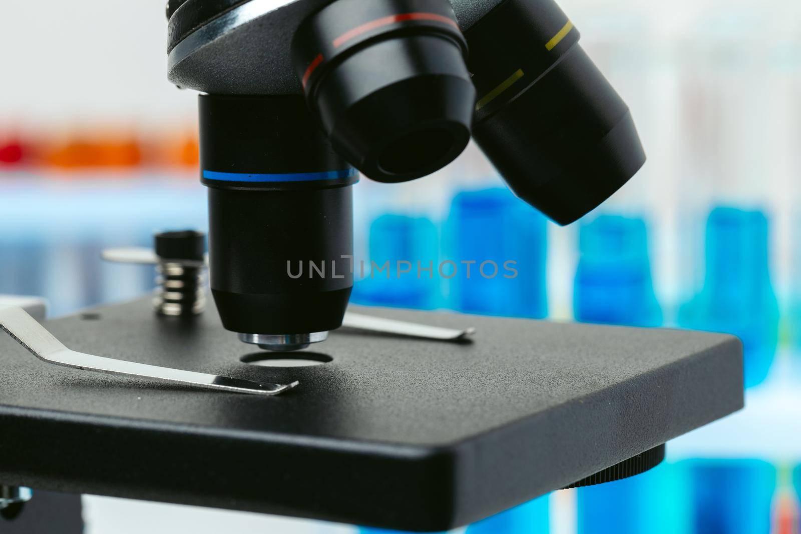 Microscope and colored test tubes on table in laboratory, close up