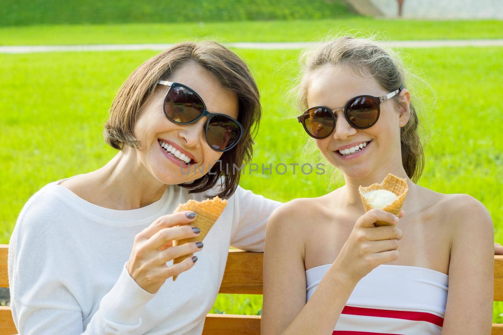 Holiday with the family. Happy young mother and cute daughter of a teenager in a city park eating ice cream, talking and laughing